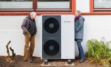 Ein Mann und eine Frau stehen neben einer großen, neu installierten Wärmepumpe und schauen sie sich an.