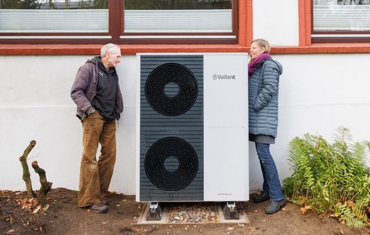 Ein Mann und eine Frau stehen neben einer großen, neu installierten Wärmepumpe und schauen sie sich an.