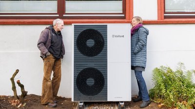 Ein Mann und eine Frau stehen neben einer großen, neu installierten Wärmepumpe und schauen sie sich an.