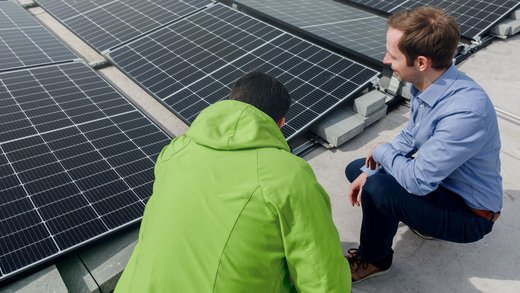 Zwei Männer hocken vor Solarmodulen und begutachten diese.