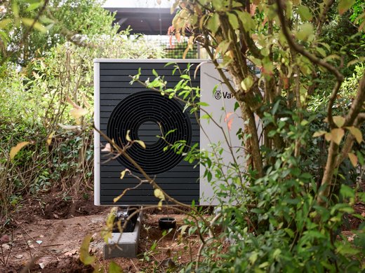 Neu installierte Wärmepumpe im Garten zwischen Gebüsch und Bäumen.