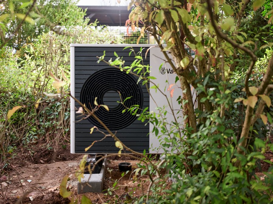 Neu installierte Wärmepumpe im Garten zwischen Gebüsch und Bäumen.