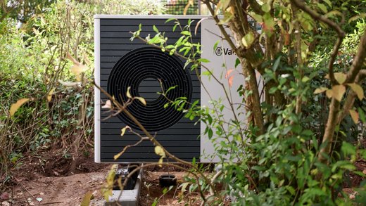Neu installierte Wärmepumpe im Garten zwischen Gebüsch und Bäumen.