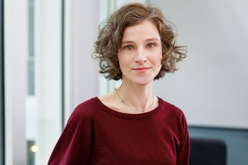 Eine Frau mit gewelltem blondem Haar in roter Kleidung blickt in die Kamera.