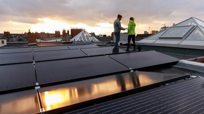 Zwei Personen hinter einem Solarkraftwerk auf einem Dach unterhalten sich.