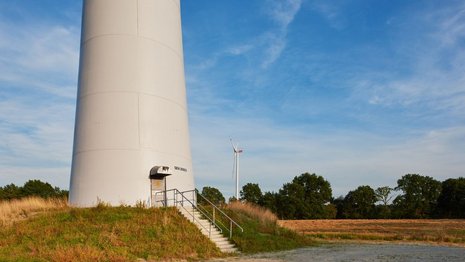 Windkraftanlage mit rotierenden Windrädern auf einem grünen Hügel.