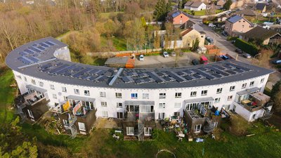 Wohnkomplex mit zahlreichen Solarpanels auf den Dächern, umgeben von Gärten und angrenzenden Wohnhäusern.