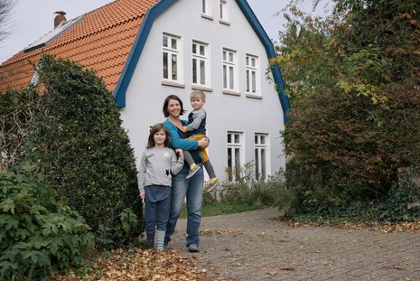 Eine Frau und zwei Kinder vor einem alten Bauernhaus mit sanierter Fassade.
