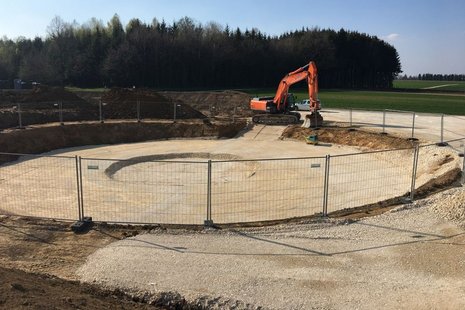 Rundes Erdloch mit Bagger bei der Arbeit im Hintergrund.