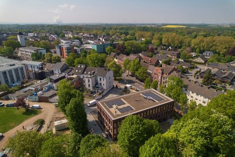Luftbild von einem Ort in dessen Zentrum ein großes Rechteckiges Gebäude steht. Das Dach des Gebäudes ist völlig von Solarmodulen belegt.