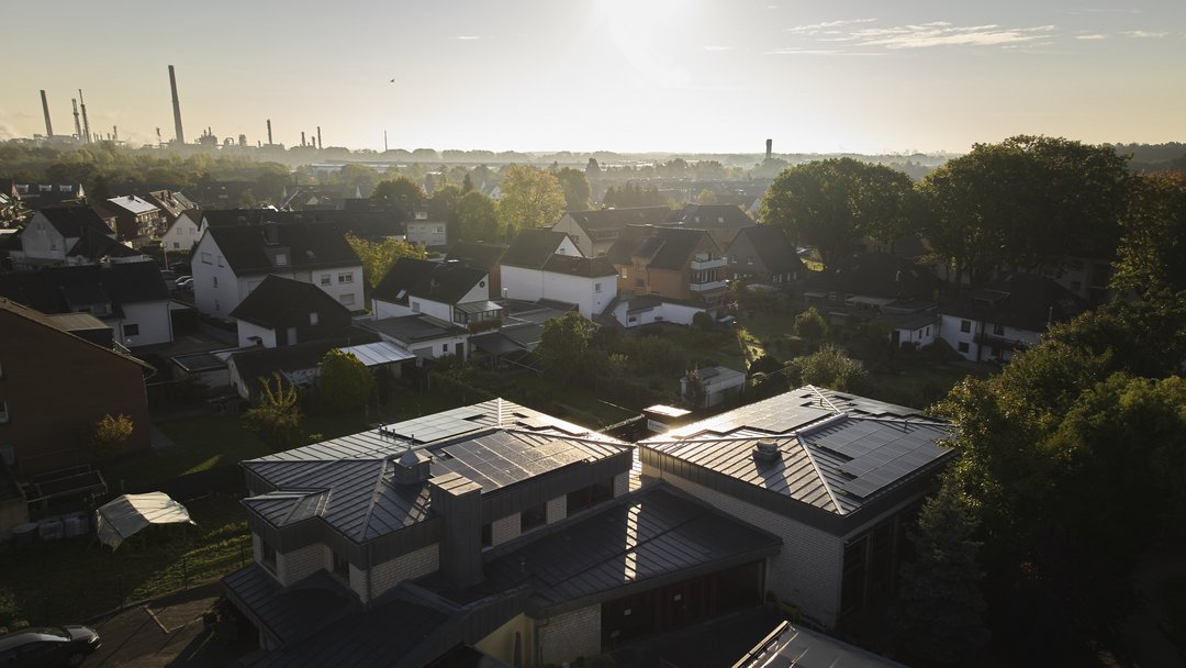 Kirchengebäude mit Photovoltaik-Solaranlagen auf den Dächern in einem Wohngebiet, im Hintergrund ist in weiter Entfernung ein Kraftwerk zu sehen.