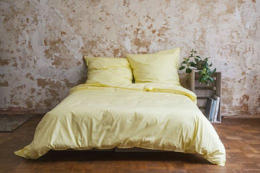 Freistehendes Bett mit Decke und 2 Kissen in heller Bettwäsche.