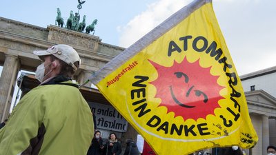 Person hält eine Fahne mit der Aufschrift "Atomkraft? nein danke" vor dem Brandenburger Tor in Berlin hoch.