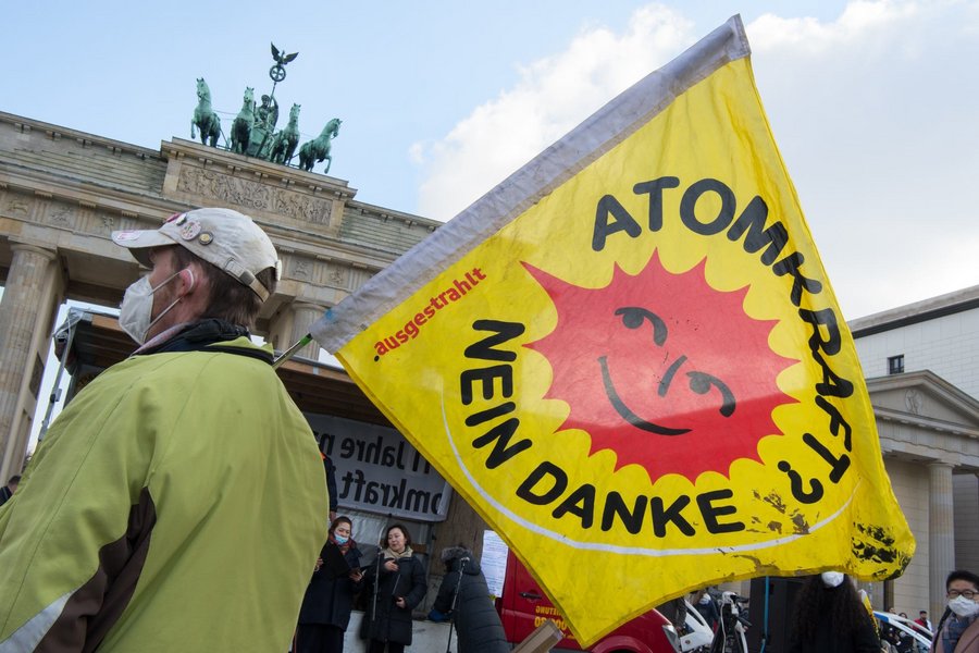 Person hält eine Fahne mit der Aufschrift "Atomkraft? nein danke" vor dem Brandenburger Tor in Berlin hoch.