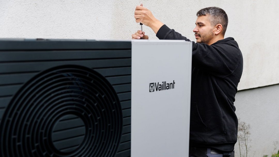 Ein Mann in schwarzem Hoodie schraubt mittels Schraubendreher oben an einer Vaillant Wärmepumpe.