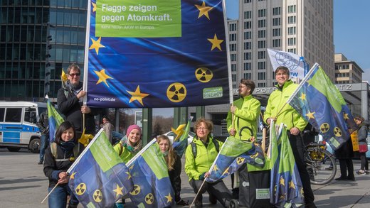Demonstranten halten die Fahnen der Europäische Union hoch. Zwei Sterne sind durch das Symbol der nuklearen Gefahr ersetzt. Die Fahnen tragen die Aufschrift "Flagge zeigen gegen Atomkraft".