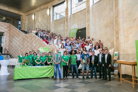 Gruppenfoto der Kongress-Teilnehmenden auf einer breiten Treppe im Kongressgebäude. Das Team von Greenpeace Energy steht in grünen T-Shirts hinter ihrem Empfangstresen dabei.