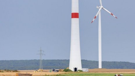 Fernaufnahme eines Feldes mit zwei Windturbinen und einem Strommast in der Mitte.
