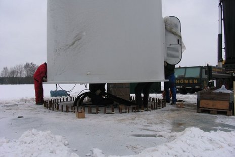 Windkraftanlage: Mast wird errichtet, Arbeiter montieren Teile.