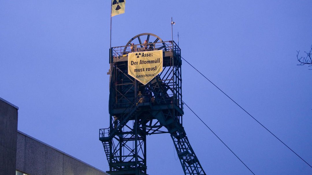 Auf einem Förderturm aus Stahl hängt ein Transparent von Greenpeace mit dem Text "Asse: Der Atommüll muss raus!"