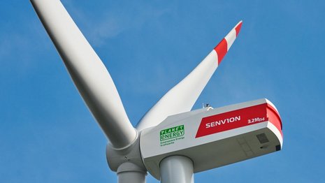 Nahaufnahme eines Windturms. Im Hintergrund ein klarer Himmel.