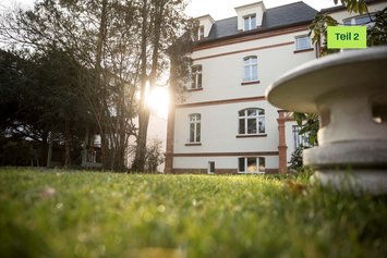 Eine alte Villa umgeben von grüner Wiese. Die Perspektive ist von unten, von der Wiese aus.
