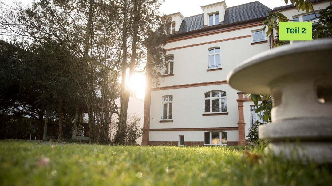 Eine alte Villa umgeben von grüner Wiese. Die Perspektive ist von unten, von der Wiese aus.