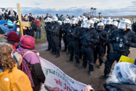 Eine Gruppe Demonstranten steht einer Gruppe vermummter Polizisten in Schutzanzügen gegenüber.