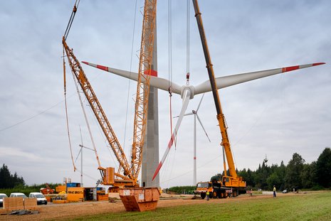 Montage der drei Flügel am Mast der Windkraftanlage mit zwei gelben Kränen.