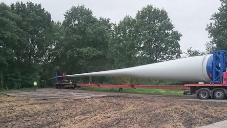 Ein Fahrzeug transportiert ein Windradblatt über ein Feld.