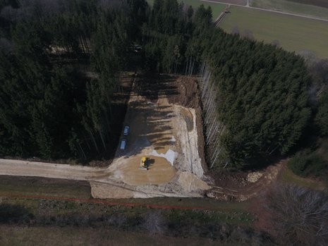 Ein Waldstück aus Vogelperspektive. Ein Teil des Waldes ist abgeholzt. Ein Bagger gräbt den Boden um.