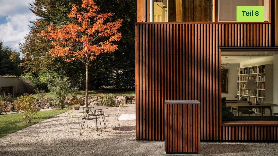 Modernes Haus mit Holzpaneelen als Außenwand. Links ist eine gelbe Sprechblase mit dem Text "Blogserie Teil 8" eingesetzt.