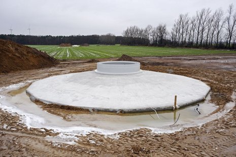 Fundament einer Windkraftanlage im Vordergrund und kultiviertes Feld im Hintergrund.