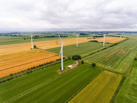 Blick von oben auf mehrere Windkraftanlagen, die in Mitten eines ländlichen Gebiets stehen