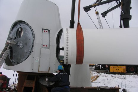 Montage eines Windradflügels. Ein Arbeiter überwacht die Installation.