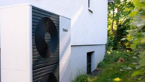 Eine weiße Wärmepumpe mit der Aufschrift Vaillant an der Außenwand eines frei stehenden Wohnhauses.