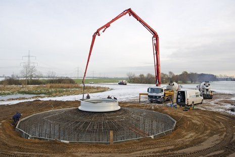 Fundamente einer Windkraftanlage mit einem gelben Lastwagen mit rotem Arm im Hintergrund.