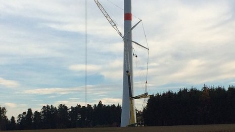 Vor einem im Bau befindlichen Windkraftturm steht ein Kran