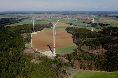 Windkraftanlage von oben in Naturlandschaft vor einem bewaldeten Gebiet