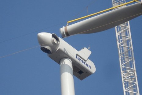 Aufnahme von unten bei der Montage eines Windradblattes am Rotor mit einem weißen Kran.