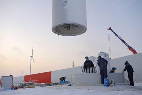 Die Windradwelle wird errichtet. 4 Arbeiter beaufsichtigen den Vorgang.