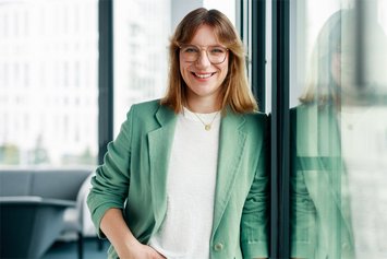 Frau in weißem T-Shirt und grauer Jacke schaut in die Kamera.