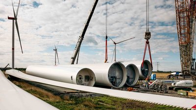 Große Rotorblätter und mehrere Turmsegmente einer Windkraftanlage liegen zur Montage bereit.