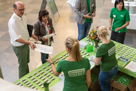 Mitarbeiterinnen von Greenpeace Energy in grünen T-Shrts mit Logo vergeben an einem Stand Namensschilder