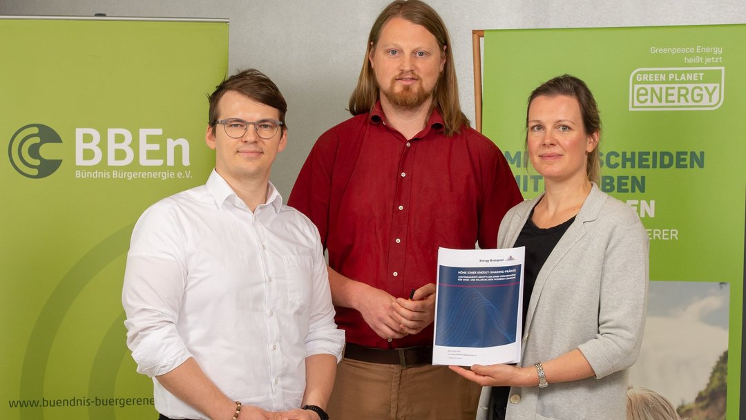 Zwei Männer und eine Frau, die ein DINA4 großes Papier sichtbar hochhält, stehen nebeneinander und blicken in die Kamera