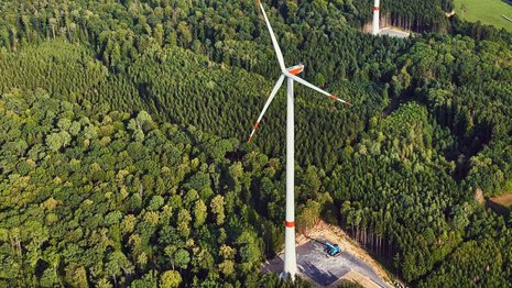 Windräder im Wald vom Himmel aufgenommen. Unten sind kleine Bauflächen mit Baugeräten zu sehen.