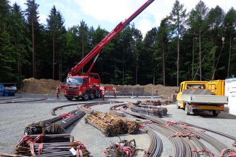 Ein Kran hebt Stahlstangen auf einer Baustelle.