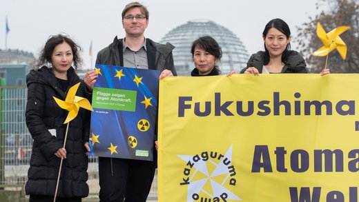 4 Personen halten ein gelbes Transparent mit der Aufschrift "Fukushima" und eines mit der europäischen Flagge hoch, auf dem zwei Sterne durch das Symbol für die nukleare Gefahr ersetzt sind.