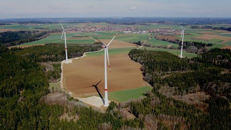 Windkraftanlage von oben in Naturlandschaft vor einem bewaldeten Gebiet