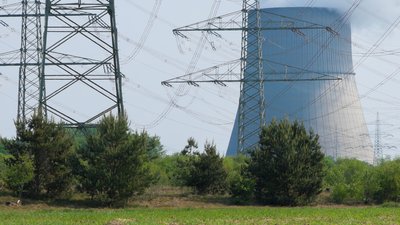 Feld mit einem Atomkraftwerk und Freileitungmasten im Hintergrund.